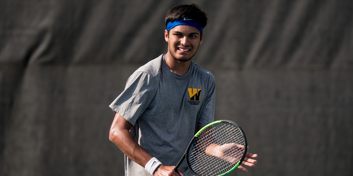 College tennis player holding a racquet in his hand smiling.