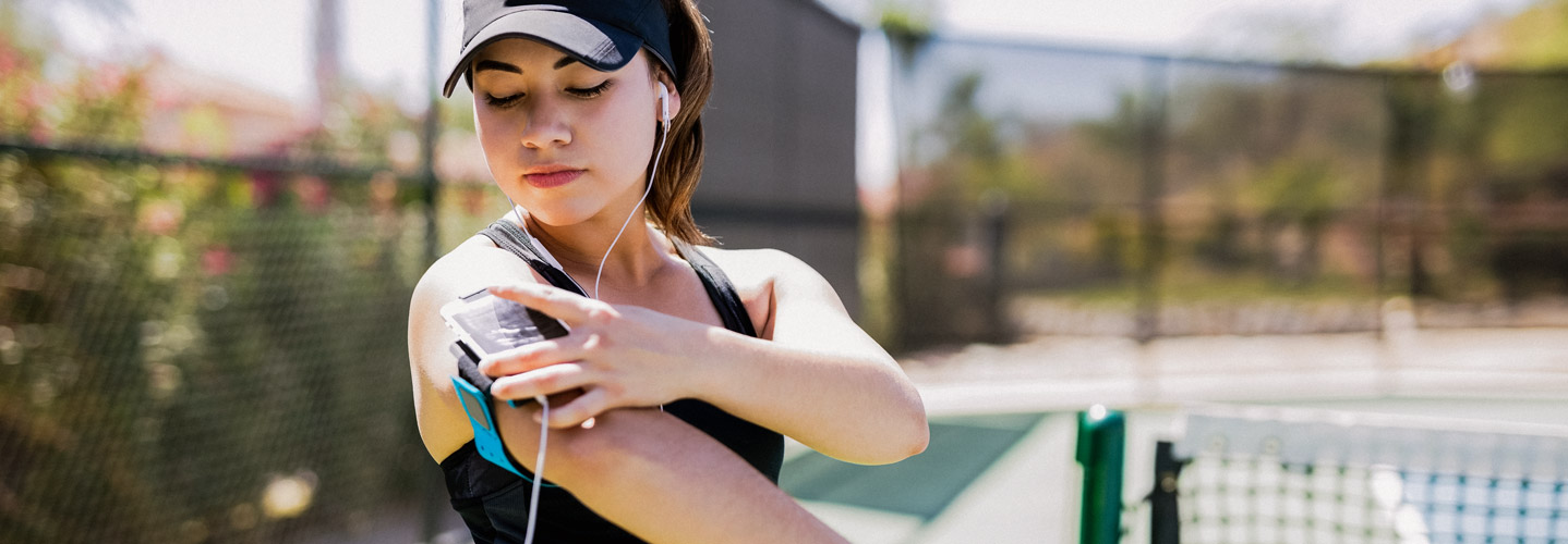 Female tennis player setting up headphones and armband holding phone.