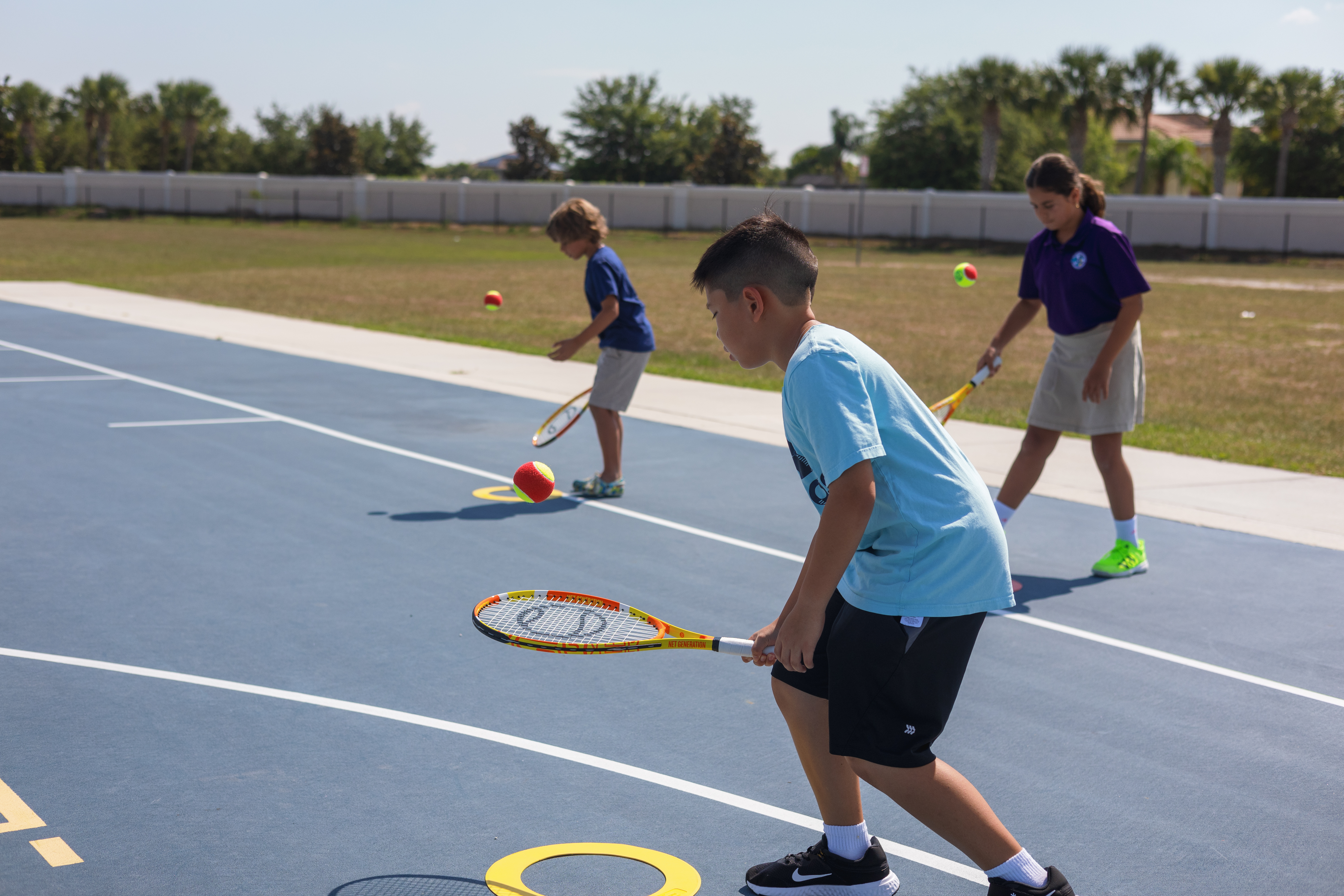 School children running tennis drills to learn how to play on an outdoor court.