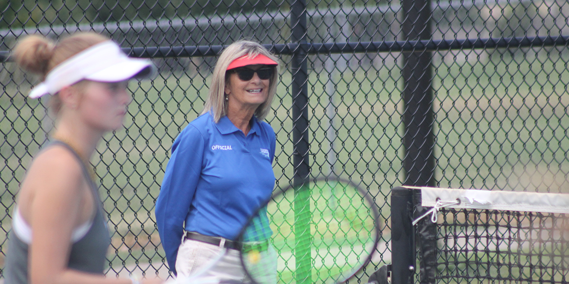 A female official officiates a match from next to the net post.