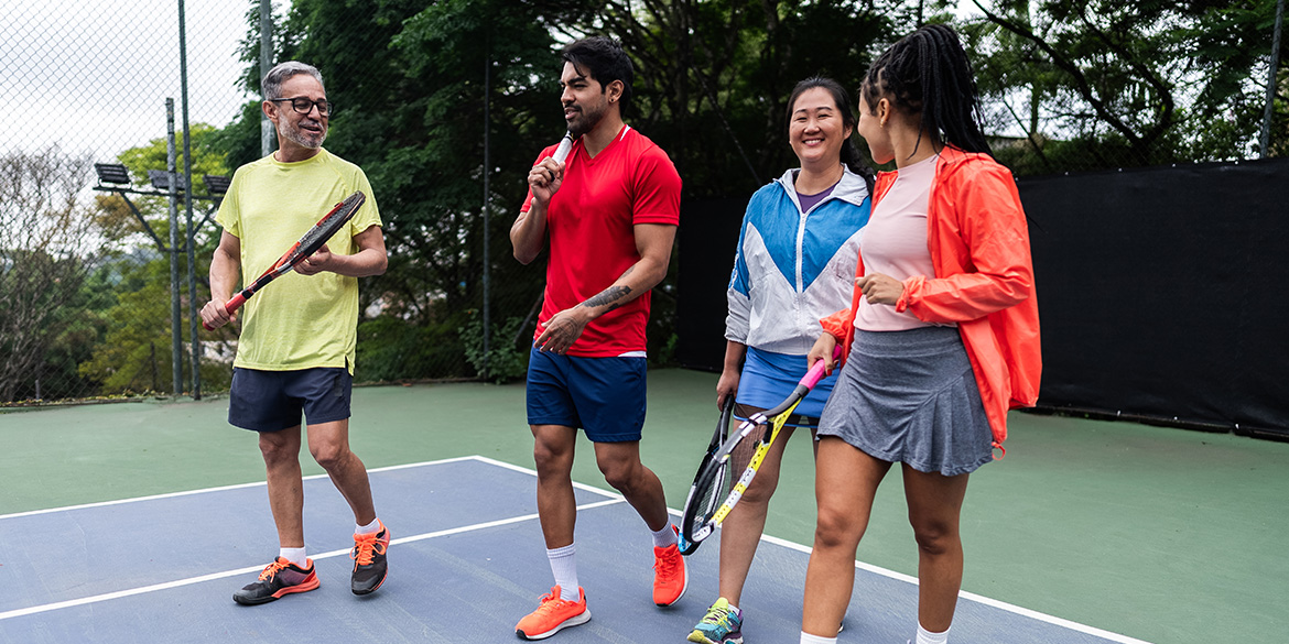 Adult tennis players on a court talking with racquets in hands.