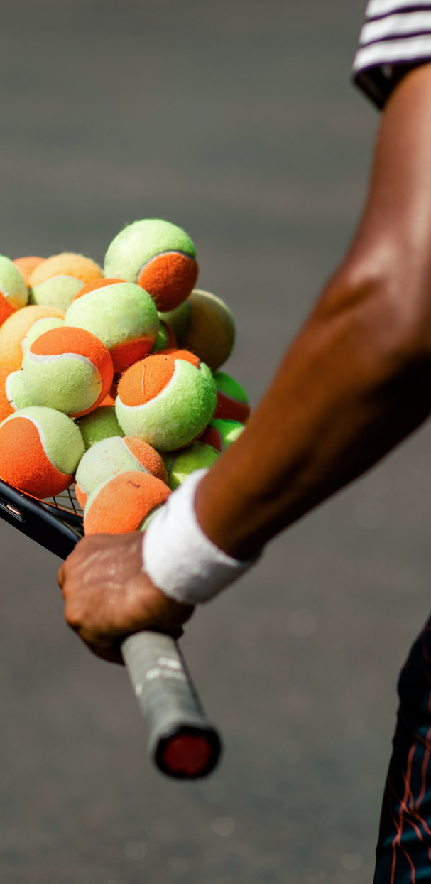 Men's arm holding a bunch of orange tennis balls on a racquet.