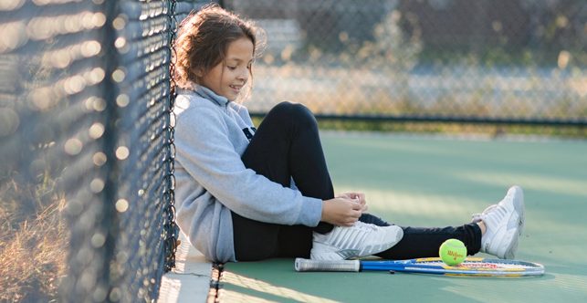 Young girl sitting with tennis racquet and balls on a court.