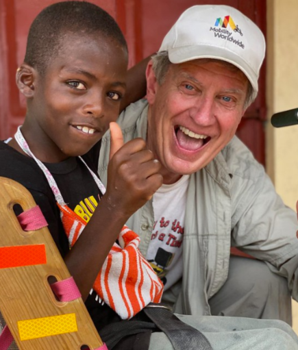 Gary Moreau on right poses with a young African-American boy who is sitting on a mobility cart.