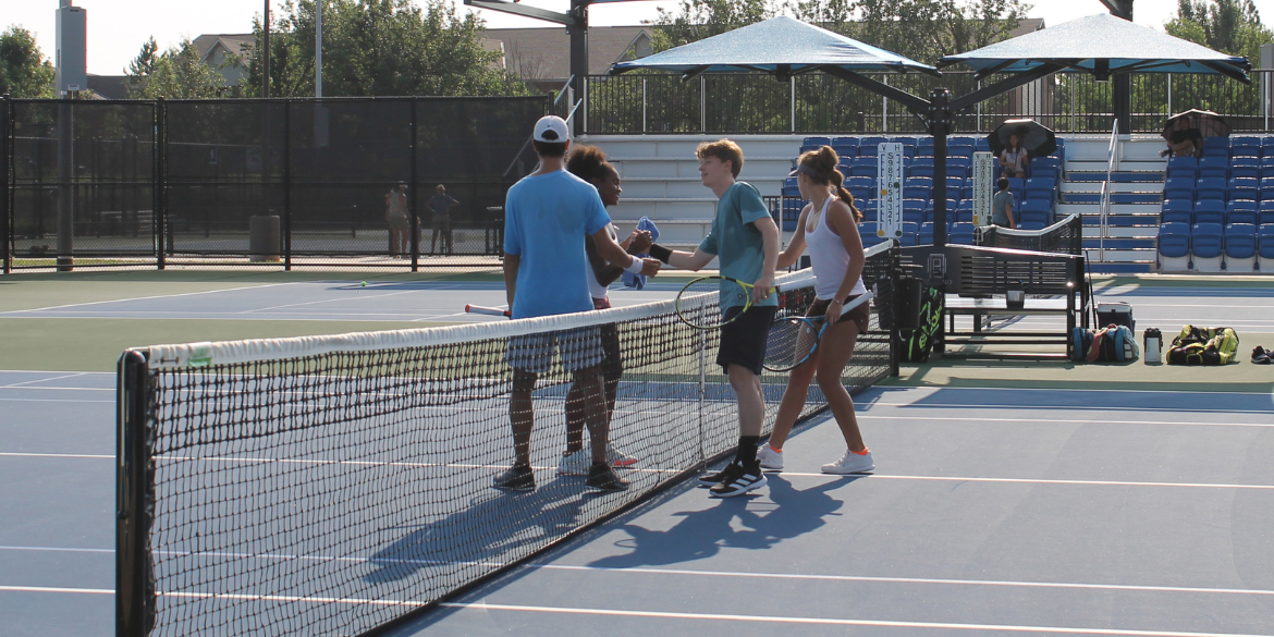 A group of four tennis players shaking hands after a doubles match.