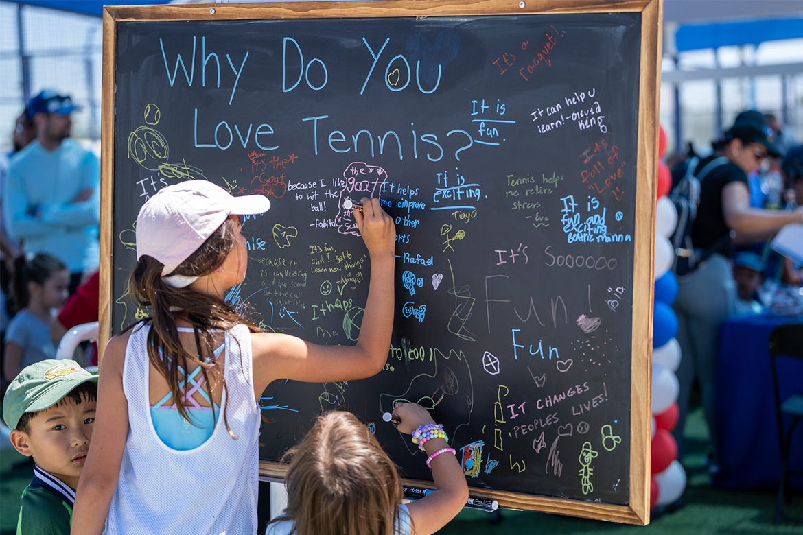 Kids write what they love about tennis on a chalkboard.
